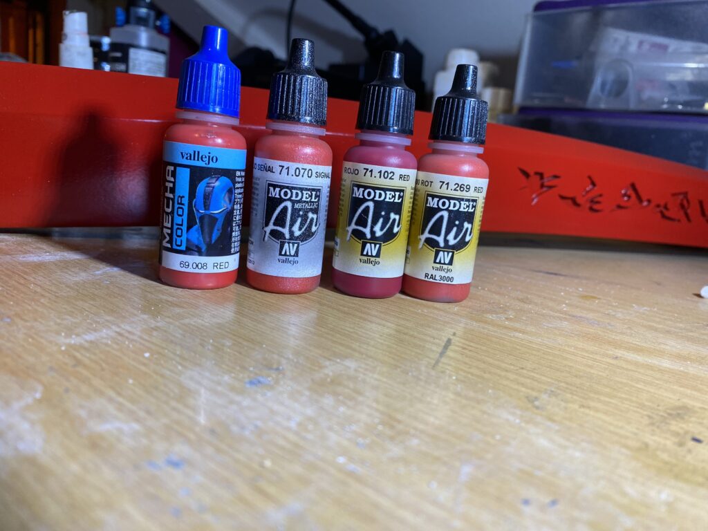 Four red airbrush paints, sitting in a line. FOUR RED AIRBRUSH PAINTS SITTING IN A LINE.