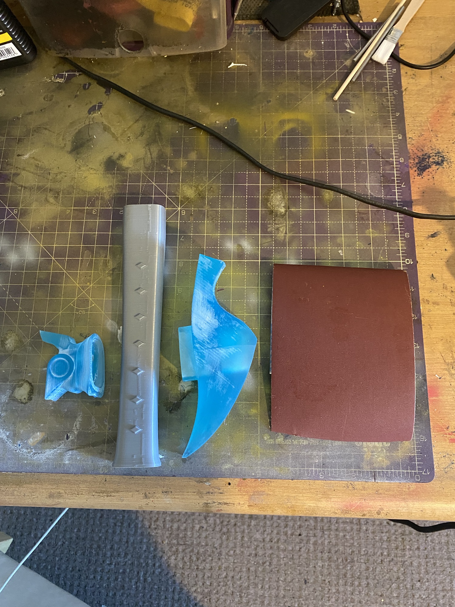 The Wind Sword's pommel, handle and hilt on a work surface next to sandpaper.