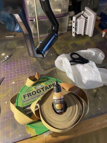 Handle of the longshot hanging above some frog tape, leather strips and a carrier bag next to some scissors.